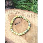 Bijou bracelet serpentine vert-jaune sur tranche de bois, harmonie intérieure et détente émotionnelle.