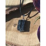Pendentif tourmaline noire brute sur rondin avec cordon noir et feuilles violettes en arrière-plan, pierre naturelle associée à la stabilité, au recentrage et à la protection énergétique.