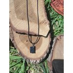 Pendentif en tourmaline noire brute posé sur tranche de bois avec décor végétal, bijou en pierre naturelle évoquant le recentrage, la clarté intérieure et la protection douce.