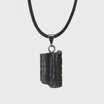 Pendentif tourmaline noire brute sur fond blanc avec cordon noir et bélière acier inoxydable, pierre naturelle reliée au recentrage, à la force calme et à l’équilibre intérieur.