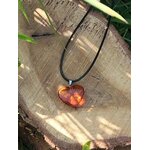 Pendentif cœur en ambre naturel sur cordon noir, posé sur une tranche de bois au soleil, bijou lumineux relié au réconfort, à la sérénité et à l’énergie positive.
