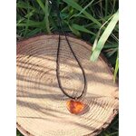 Pendentif cœur d’ambre posé sur rondin de bois, bijou aux tons miel associé à la sérénité, à la stabilité intérieure et à la chaleur réconfortante.