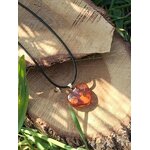 Pendentif cœur en ambre naturel parmi des feuilles vertes au soleil, bijou aux teintes chaudes associé à la douceur, au réconfort et à la lumière intérieure.