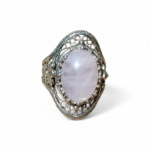 Bague en quartz rose cabochon montée sur argent 925 au design travaillé, posée sur fond clair minimaliste, lumière douce révélant ses reflets laiteux, évoquant apaisement, amour de soi et équilibre émotionnel.