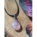 Pendentif goutte en quartz rose sur cordon noir, présenté sur tranche de bois, bijou naturel lié à la sérénité, à l’écoute de soi et à la douceur du cœur.