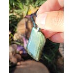 Pendentif labradorite verte tenu en main, reflets bleu-vert, décor galets – protection