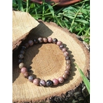 Bracelet rhodonite 6 mm sur rondin de bois au soleil avec herbes vertes, pierre naturelle pour réconfort émotionnel, tendresse intérieure et apaisement du cœur