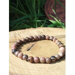 Bracelet rhodonite 6 mm sur support en bois avec herbes en fond et lumière chaude, confiance retrouvée, stabilité du cœur et douceur relationnelle