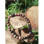 Bracelet rhodonite 6 mm sur champignons décoratifs dans l’herbe, sérénité relationnelle, chaleur du cœur et réassurance émotionnelle