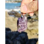 PPendentif lépidolite rectangulaire tenu à la main en bord de mer, bijou en pierre naturelle évoquant le lâcher-prise, la tendresse et la paix du mental.