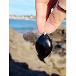 Pendentif tourmaline noire marquise tenu entre les doigts face à la mer en Bretagne, bijou en pierre naturelle évoquant l’ancrage, la protection et la maîtrise de soi.