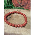Bracelet jaspe rouge 6 mm sur tranche de bois avec herbes vertes et décor ésotérique, perles rouge brique pour courage posé, ancrage et présence solide