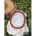 Bracelet jaspe rouge 6 mm posé sur amas de quartz blanc et bois brut, perles rouge profond, élan vital, courage et présence