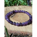 Bracelet en améthyste posé sur bois avec fond végétal, nuances violettes naturelles pour détente nerveuse, lucidité et recentrage