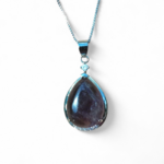 Collier pendentif en améthyste forme goutte, cabochon violet foncé sur chaîne fine, présenté sur fond clair minimaliste.