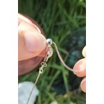 Gros plan sur chaînette réglable du pendentif goutte améthyste tenue entre les doigts, plaqué argent sur fond d’herbe