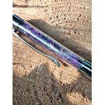 Stylo bille transparent rempli d’éclats d’améthyste violette en gros plan, posé sur une surface de bois, accessoire d’écriture en pierres naturelles pour créativité, inspiration et apaisement du mental.