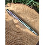 Stylo bille transparent rempli d’éclats d’améthyste violette, posé sur une grande rondelle de bois avec herbe en arrière-plan, accessoire d’écriture en pierres naturelles pour créativité, intuition et apaisement du mental.