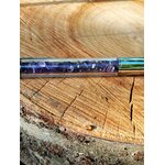 Gros plan sur le réservoir d’un stylo bille rempli d’éclats d’améthyste violette, posé sur une rondelle de bois, accessoire d’écriture en pierres naturelles pour inspiration, concentration et apaisement du mental.