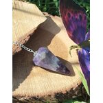 Pendule en améthyste naturelle avec chaîne argentée, posé sur une souche de bois en extérieur avec aile de papillon colorée, outil de radiesthésie ésotérique pour intuition et spiritualité.