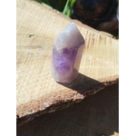 Pointe d’améthyste en pierre naturelle posée sur tranche de bois en extérieur, cristal violet évoquant la douceur du cœur, la lucidité et la paix intérieure.