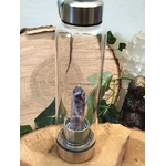 Bouteille d’eau en verre améthyste, 500 ml, sur rondin de bois décoratif, objet de lithothérapie pour allier hydratation, énergie et apaisement.