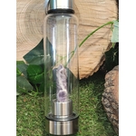 Bouteille d’eau en verre énergisante avec pointe d’améthyste naturelle, 500 ml, posée sur un décor végétal et bois brut, accessoire de lithothérapie pour l’hydratation consciente, le bien-être énergétique et l’apaisement.
