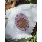 Petit galet orgonite améthyste avec fleur de vie dorée posé sur une grande géode de cristal blanc en extérieur, objet de lithothérapie pour protection énergétique, harmonisation des énergies et décoration spirituelle
