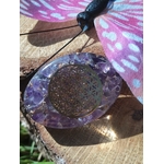 Petit galet énergétique en orgonite améthyste avec symbole fleur de vie, posé sur une planche de bois avec papillon décoratif rose et bleu, objet de lithothérapie pour protection, harmonisation des énergies et décoration spirituelle