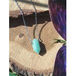 Pendentif pointe en aventurine verte sur chaîne argentée, posé sur tranche de bois avec décor naturel, bijou en pierre naturelle associé à l’apaisement, à l’équilibre émotionnel et à la douceur du cœur.