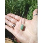 Pendentif en pointe d’aventurine verte tenu dans la main sur fond d’herbe, collier en pierre naturelle associé à la confiance douce, au calme des pensées et à l’équilibre émotionnel.