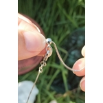 Pendentif goutte en lapis lazuli, gros plan sur la chaînette plaquée argent à réglage coulissant, tenu entre les doigts en extérieur sur fond d’herbe.