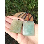 Pendentif fluorite verte rectangulaire tenu dans la main devant l’herbe, bijou en pierre naturelle évoquant le recentrage, la douceur du cœur et la lucidité.
