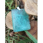 Gros plan sur pendentif rectangulaire en fluorite verte posé sur rondins de bois dans l’herbe, collier en pierre naturelle relié à la sérénité, à l’ordre des pensées et à la présence à soi.