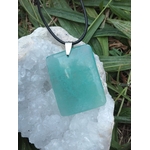 Pendentif fluorite verte rectangulaire sur cordon noir posé sur géode blanche dans l’herbe, pierre naturelle associée à l’apaisement, au lâcher-prise et à l’équilibre intérieur.