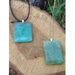 Deux pendentifs rectangulaires en fluorite verte sur cordon noir et chaîne argentée, posés sur une tranche de bois, bijoux en pierre naturelle associés à la tendresse, à la clarté et à l’équilibre émotionnel.