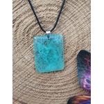 Pendentif rectangulaire en fluorite verte sur cordon noir, posé sur rondin de bois avec décor ésotérique, collier en pierre naturelle évoquant la concentration paisible, le recul et l’harmonie émotionnelle.