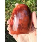 Forme libre Cornaline naturelle tenue dans la main en extérieur, pierre orange-rouge polie – soutien énergétique de vitalité, créativité et équilibre émotionnel.