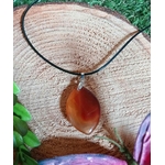 Pendentif Cornaline naturelle suspendu devant une géode blanche, bijou orange lié au chakra sacré pour vitalité, créativité et concentration