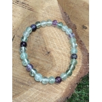 Bracelet fluorite verte et violette en perles naturelles vu du dessus sur rondin de bois, bijou Magic Gaïa pour clarté mentale et apaisement émotionnel.