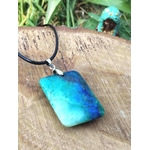 Pendentif azurite chrysocolle bleu vert sur cordon noir, posé sur bois avec herbes en arrière-plan, pierre naturelle associée à la parole fluide, à l’équilibre affectif et à la paix intérieure.