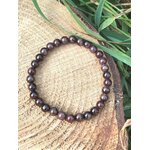 Bracelet grenat 6 mm en perles rondes bordeaux sur tranche de bois en extérieur, détermination, courage enraciné et assurance calme