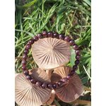 Bracelet grenat 6 mm sur champignons en bois dans l’herbe, perles rouge profond pour courage tranquille, ancrage et stabilité intérieure