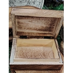 Boîte à bijoux en bois sculpté Gaïa ouverte, intérieur en bois clair, posée sur des rondins de bois avec un disque décoratif gris en arrière-plan.