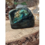 Labradorite forme libre sur rondin de bois, reflets bleu-vert et dorés, pierre naturelle associée à la stabilité, à la lucidité intérieure et à la protection subtile.
