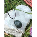 Pendentif agate mousse vert foncé sur cordon noir, posé sur galet blanc avec herbe et touche violette, recentrage doux et paix émotionnelle
