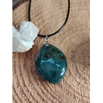 Pendentif en agate mousse poli (forme ronde) sur cordon noir, posé sur un fond en bois avec une petite géode à côté ; pierre associée au chakra cœur, réputée pour apporter apaisement, harmonie émotionnelle et connexion à la nature.