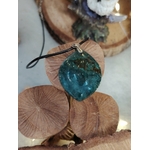 Pendentif agate mousse (goutte) sur cordon noir, posé sur galets ronds avec feuillage en arrière-plan ; pierre du chakra cœur, invite au calme et à l’équilibre émotionnel.