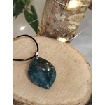 Pendentif agate mousse (goutte) sur cordon noir, posé sur support en bois avec feuillage ; favorise apaisement et ancrage naturel.