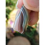 Pendentif agate du Botswana à bandes grises et roses en gros plan dans la main, sérénité émotionnelle et présence apaisée